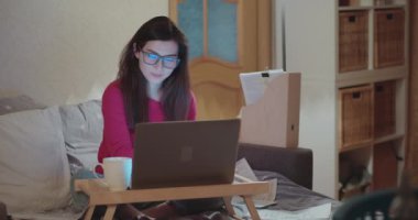 Çevrimiçi ders izleyen genç bir öğrenci ve karantinaya alınırken evden ders çalışıyor. Bilgisayar ekranına bakarken not alan genç bir kadın. Tecritteki kız serbest. Sosyal uzaklık kavramı.