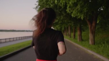 Kırmızı şortlu genç esmer nehir kıyısında koşuyor. Parkta koşan bir kadın. Yalnızlıktan ve sağlıklı yaşam tarzından hoşlanan bir kız. Solo aktivite kavramı, spor, maraton.