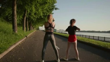 Genç seksi çok ırklı kadınlar nehir kenarında koşmadan önce kaslarını esnetiyorlar. Güzel kızlar kollarını ve bacaklarını ovalarlar. Eğitimden önce ısın. Sağlıklı yaşam tarzı kavramı