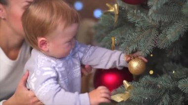 Genç esmer anne ve küçük bebeği Noel arifesinde evde Noel ağacı süslüyorlar. Ebeveynlik ve birliktelik kavramı. Güzel bir kadın yeni yıl tatilinde bebeğini okşuyor..