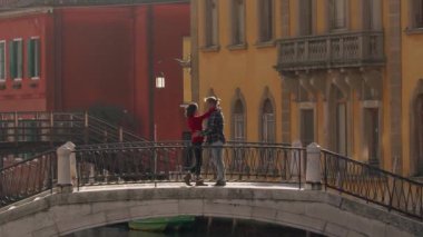 Yakışıklı bir adam, balayı sırasında Venedik köprüsünde duran Asyalı sevgilisini öpüyor ve sarılıyor. Tatili geçirmenin en iyi yolu Avrupa 'ya seyahat etmek..