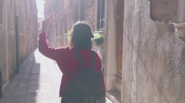 Maceracı Asyalı kadının Venedik, İtalya 'da akıllı telefonuyla küçük rahat caddelerin videosunu kaydettiği arka manzara. Kadın sırt çantası Instagram 'ı için ilginç materyaller hazırlıyor. Blogger hayatı
