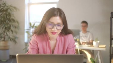 Güzel Asyalı iş kadını, gözlüklü, ofis masasında dizüstü bilgisayarının önünde oturuyor, kollarını kaldırıyor ve başarılı iş terfisini kutluyor. Mutlu ofis çalışanı şerefe.