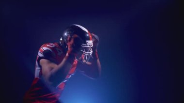 Parlak stadyum ışıkları altında kasklı kararlı profesyonel Amerikan futbolcusunun portresi topu yakalıyor. Üniformalı kendinden emin bir adam. Usa takım oyunu ve ekstrem spor ruhu konsepti.