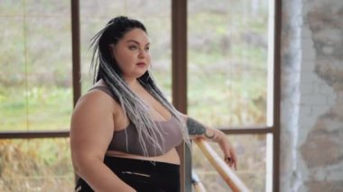 Rasta saçlı mutlu vücutlu şişman kadın spor salonunda esneme hareketleri yapıyor. Doğal güzellik ve spor anlayışı. Şişman kadın izole edilmiş egzersizler yapıyor. Rahatlama sükunet konsepti