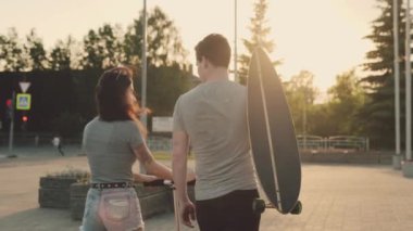 Arkadaşlar birbirleriyle iletişim kuruyor ve gülüyorlar. Güzel bir kız ve çekici bir adam kaykay ve scooterla meydanda gün batımına doğru yürüyorlar. Aktif yaz ve üniversite hayatı.