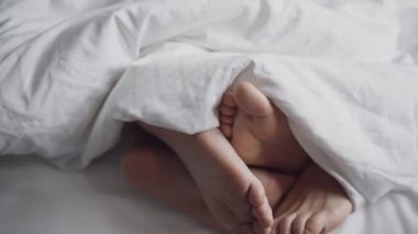 Birbirine dolanmış erkek ve kadın bacaklarının ya da ayaklarının beyaz battaniyenin altında hareket edişinin üst görüntüsü. Erkek ve kadın sabahları sevişiyor ya da yatak odasında sevişiyor. Erotik, zevk konsepti.