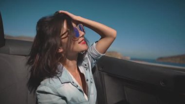 Cabriolet 'in yolcu koltuğunda oturan çekici genç kız muhteşem Akdeniz kıyısından geçiyor. Yaz rüzgarı dalgalı saçlarıyla gülen bir kız. Seyahat, tatil, macera kavramı.