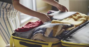 Genç kız seyahat için hazırlanıyor. Giysilerini ve laptopunu sarı bir bavula koyuyor. Seyahat kavramı, macera. Güzel dövmeli bir bayan seyahatten önce gerekli şeyleri toplar..