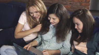 Koltukta ya da koltukta oturup dizüstü bilgisayara bakıp gülen çok ırklı insanlar. Çekici kadın arkadaşlar bilgisayar başında birlikte vakit geçiriyorlar. Evde birlikte vakit geçirme kavramı.