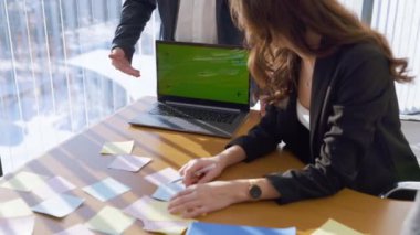 İş arkadaşlarının masa başında yaklaşan projeleri tartıştığı bir ofis sahnesi. Meslektaşlar dizüstü bilgisayardaki sunum planı hakkında fikir alışverişinde bulunuyorlar. Takım çalışması kavramı, teknoloji.