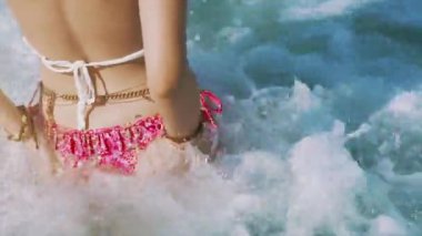 Bikinili genç bir kadın geri çekiliyor ve deniz dalgalarında su sıçrıyor. Tropikal adada ince kalça ya da kalça güneş banyosu. Güzellik, tatil ve yaşam tarzı kavramı. Cennet sahili