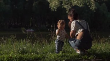Anne ve bebeğinin parkta güzel bir sahnesi. Anne bebeğe çiçek veriyor ve çocuk el sallıyor. Etraftaki dünyayı öğrenen, doğayı deneyimleyen çocukların duygusal portresi. Bekar anne kavramı.