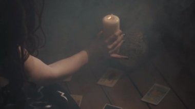 Karanlık odada dumanla gizemli ayinler yapan bir kadın. Falcı elinde mum ve masada tarot kartlarıyla arınma hareketi yapıyor. Kaderi ve geleceği tahmin eden kadın..