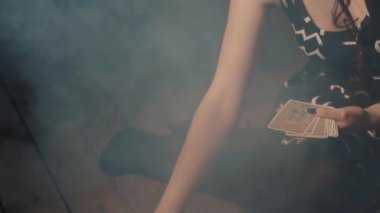 Ezoterik ayin sırasında tarot kartları yerleştiren bir kadın. Falcı kartları koyarak kaderini tahmin ediyor. Arka planda yanan mum, duman ve kafatası olan ürkütücü mistik bir atmosfer. Kehanet kavramı.