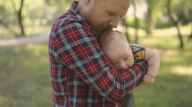 Elinde bebekle dışarıda yürüyen mutlu bir adam. Babam parkta yürürken neşeyle bebeği kucağına aldı. Çocuk aydınlık yaz gününde ailesiyle birlikte dünyayı keşfediyor..