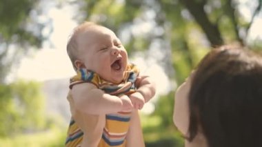 Mutlu anne, oynamak ve dünyayı gezdirmek için ellerini havaya kaldırıp çocuğu kaldırıyor. Çocuk ve ebeveyn birlikte parkta yürürken gülümsüyor. Anne ve bebek birlikte oynuyorlar..