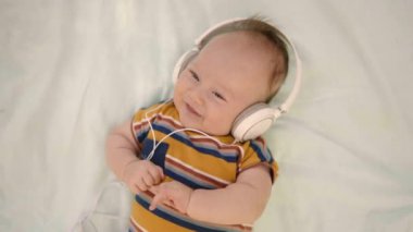 Başında kulaklıklarla battaniyeye uzanmış sevimli bebek manzarası. Gülümseyen çocuk dünyayı müzikle deneyimliyor. Çocuk çok ilgili ve sakin görünüyor, aile yürüyüşü sırasında dinleniyor..