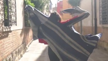 Çekici genç Asyalı kadın şık kırmızı bir kazak giymiş çizgili pançosunu sallıyor ve öpücük yolluyor. Küçük bir sokakta koşuşturan ve İtalya 'da maceralara hazır eğlenceli bir kız..