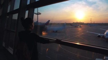 Genç bayan gezgin, boş zaman ya da iş yeri büyük uluslararası havaalanı merkezinin cam penceresinin yanında duruyor, gündoğumu arka planı. Boş havaalanı terminali kapalı salon, yalnız bayan yolcu bekliyor.