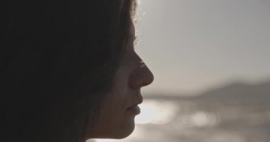 Dramatik kadın portresi. Rüzgarlı bir günde gözleri kapalı bir kadın, sinema kamerasında çekilen, dağların ve okyanusun arka planına karşı siyah takım elbiseli zalim bir kız. Güzel esmer, omzuna dokunuyor.