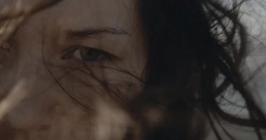 Çok yakın dramatik bir kadın portresi. Üzgün gözler ve rüzgarlı hava, sinema kamerasında çekilen, dağların ve okyanusun arka planına karşı siyah takım elbiseli zalim kız. Güzel esmer, omzuna dokunuyor.