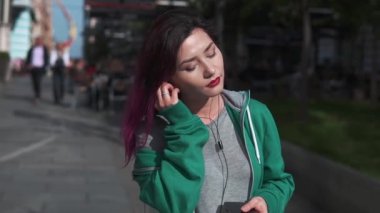 Renkli saçlı, kulaklıkla müzik dinlemekten hoşlanan akıllı telefon kullanan çekici bir genç kadın. Parlak görünüşlü gülümseyen kız aletler kullanıyor..