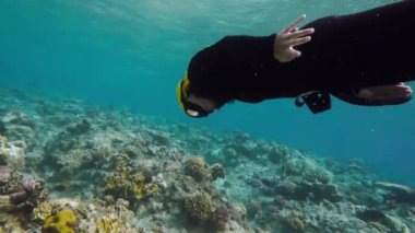 Suyun altında yüzen kız. Siyah dalış kıyafetli genç bayan dalgıç derinlikleri fethediyor. Su altı dünyasının güzelliği. Çevreyle bağlantı. Denizin derinlikleri ve egzotik. Etkin dinlenme kavramı