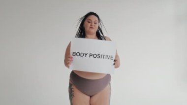 İç çamaşırlı mutlu şişman kadın elinde pozitif vücut posteri tutuyor. Sweamwer 'daki şişman kız kameraya gülümsüyor. Çeşitli güzellik, çeşitlilik hoşgörü konsepti.