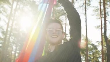 Homoseksüel bir adam güzel bir yaz gününde gökkuşağı bayrağı sallıyor. Kalp gözlüğü takan mutlu adam haklarını gösteriyor. LGBTQI, Gurur Etkinliği, LGBT Gurur Ayı, Eşcinsel Onur Sembolü