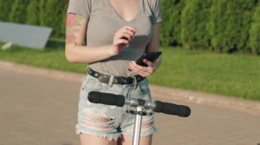 Güzel Asyalı kız akıllı telefondaki uygulamayla scooter 'ı kiralıyor. Kadın akıllı maaşla elektrikli scooter kiralıyor. Ekolojik toplu taşıma. Üniversite eko hayatı, aktif yaşam tarzı ve kiralama kavramı