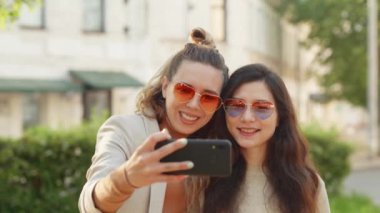 İki genç, gülümseyen hippi sarışın kadın akıllı telefondan kendi portresini çekiyor. Sokak geçmişinde çok şık kızlar var. Olumlu duygular ve aşk.