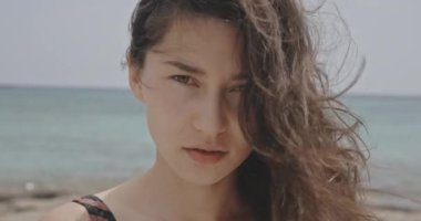 Güneşli bir günde, sahilde gülümseyen güzel bir kız portresi denize doğru yürüyen çekici genç bir kadın. Doğal manzaranın arka planında ince bir kız. Esmer, uzun saçlı.