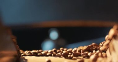 Kavrulmuş kahve çekirdekleri uçar ve ağır çekimde siyah bir arka planda döner. Taze kızarmış kahve çekirdekleri üretim fabrikası. Soğutma tabağında hazır kahve çekirdekleri..