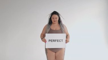 İç çamaşırlı mutlu şişman kadın elinde pozitif vücut posteri tutuyor. Doğal mükemmel değil. Çeşitli gerçek güzellik, çeşitlilik, kusurlu tolerans konsepti. Cesur kız kameraya gülümsüyor..