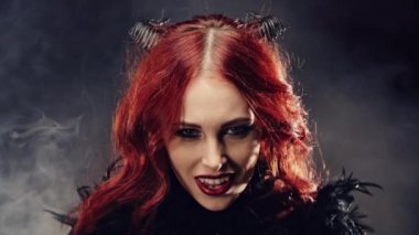 Kızıl saçlı ve şeytan boynuzlu bir cadı portresi. Kadın şeytani bir şekilde gülümsüyor ve gülüyor. Karanlık güçler tarikatı, şeytan çağırma ayinleri, cadılar bayramı, okültizm, ezoterik.