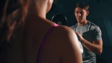 Genç esmer boksör ve antrenör. Atletik kız antrenörle tek başına çalışıyor. Erkek ve kadın kardiyo çalışması yapıyor. Adam kıza antrenman için yardım ediyor. Antrenman, güç, spor salonu kavramı.