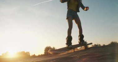 Genç, sportif bir kadın kumsalda kumda zıplıyor. Gün batımında snowboard 'a atlamaya çalışırken gülümseyen ve eğlenen bir kız. Spor konsepti, yaşam tarzı, kum kayağı, aşırı