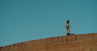 Seksi kız uçurumun kenarından kum kayağı ya da snowboard 'a binmeye hazırlanıyor. Sarışın, yolculuktan önce gemide kilit hazırlıyor. Spor, eğlence, risk, aşırı, yaz.