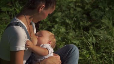 Parkta emziren bir çocuğun portresi. Yeşil ağaçlarla çevrili bir bebeğin anne göğsünü içtiği duygusal sahne. Toplu beslenmenin modern ilerici yaşam tarzı. Annelik kavramı.