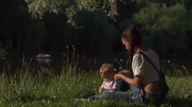 Doğanın güzelliğini yaşayan çocuk: yeşil ağaçlar, kuşlar ve su. Anne ve oğlu parkta göletin kenarında oturuyorlar. Toddler annenle el çırpmaya çalışıyor, etrafa bakıyor. Annelik kavramı