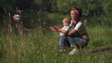 Yeni yürümeye başlayan çocuk, annenle birlikte doğanın güzelliğini deneyimleyerek hayrete düştü. Yeşil ağaçların ve suyun yaz arkaplanı. Göletin yanında bebekle birlikte genç bir annenin portresi. Annelik kavramı, aile.