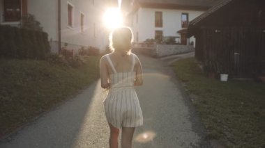Köyde yol ya da patikada yürüyen Asyalı genç bir kızın arka görüntüsü. Beni takip edin. Mutlu kadın yazın dışarıda vakit geçiriyor. Bir kadın gün batımında doğada yürür. Yaşam tarzı, seyahat, özgürlük kavramı.