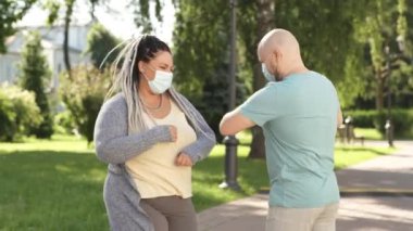 Salgın hastalık konsepti. Tıbbi maskeli iki mutlu arkadaş yaz zamanı parkta bankta oturup konuşarak sosyal mesafeyi koruyorlar. Çiftler koronavirüsün yayılmasına engel olurlar..