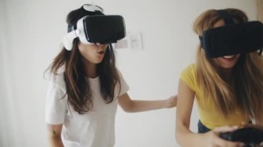 Evde sanal gerçeklik kasklı güzel kızlar var. Modern sanal gerçeklik kulaklıklarıyla video oyunları oynayan ve birlikte eğlenen iki kadın. Üç boyutlu teknoloji. Sanal gerçeklik, oyun, arkadaşlık kavramı.