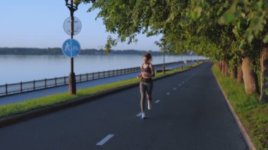 Güzel sporcu kadın maratona hazırlanıyor. Rıhtım boyunca sabah koşusu. Sokakta ya da güneş doğarken parkta egzersiz yapmak. Koşucu kardiyo yapıyor. Sağlık ve sağlıklı yaşam tarzı kavramı.