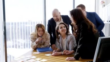Masada beyin fırtınası yapan genç yöneticilerin toplu portresi. Meslektaşlar gelecek sunumun detaylarını neşeyle tartışıyor ve yeni fikirleri dile getiriyorlar. Takım oluşturma kavramı, atmosfer.
