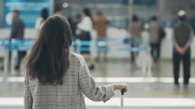 Havaalanı terminalinin ortasındaki genç iş kadınının arka görüntüsü. İş gezisi sırasında bavullu bir kadın bekliyor. İş için seyahat eden, uçuş için kayıt bekleyen bir kız..