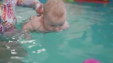 Siyah beyaz mayo giymiş mutlu anne ve bebek yüzme havuzunda eğlenerek suyun üstünde sörf yapıyor. Sağlıklı bir yaşam tarzı, aktif bir ebeveyn, çocuklarla kapalı havuzda yüzme dersleri.