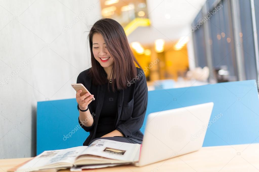 Asian college student sitting with laptop, book and phone